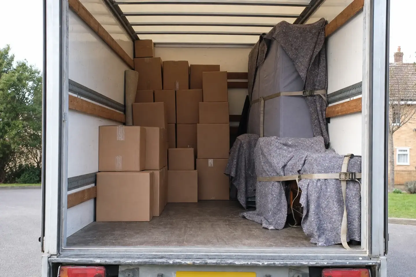 The back of a removal truck part-loaded with neatly stacked boxes and blanket-wrapped furniture strapped to one side, room left for a backload