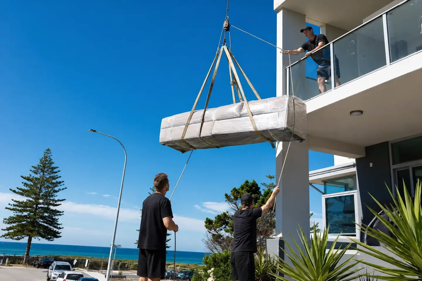 Perth removalists hoisting a large wrapped sofa up to a second-floor apartment balcony in Scarborough using lifting straps