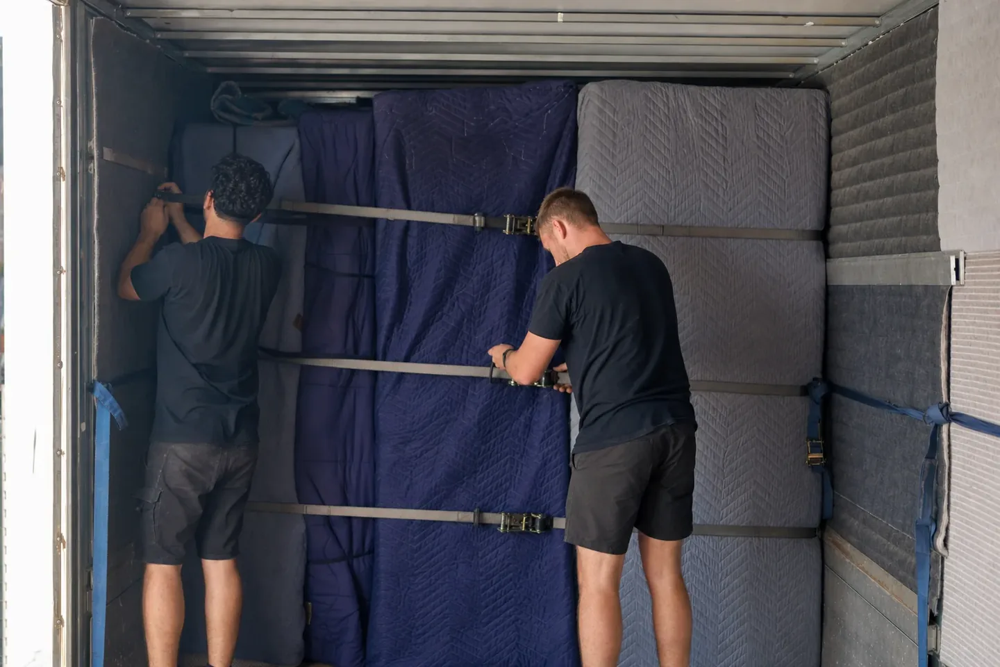 Two Perth removalists strapping and securing blanket-wrapped furniture tightly against the truck wall for a long interstate trip