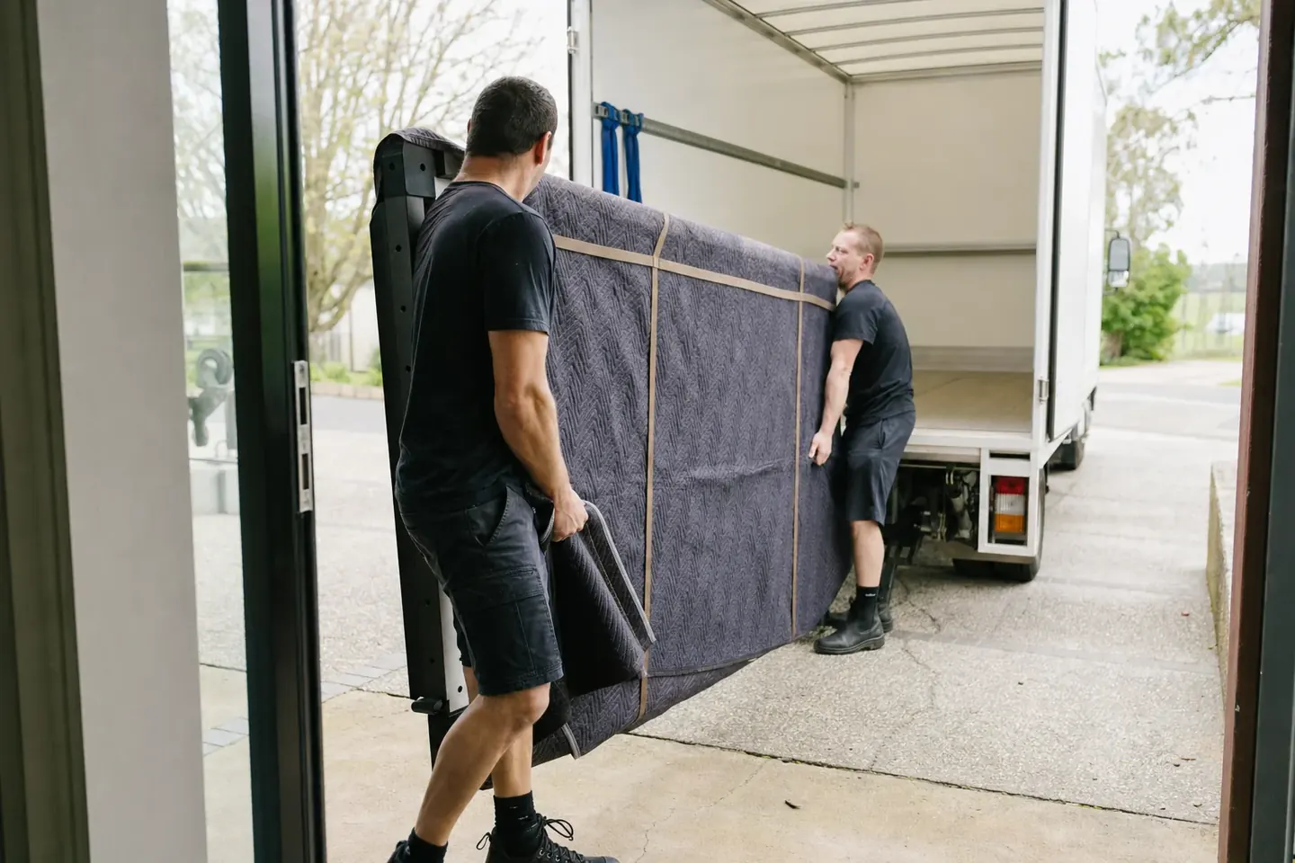 Two Perth removalists carrying a heavy blanket-wrapped slate pool table panel through a doorway to the truck